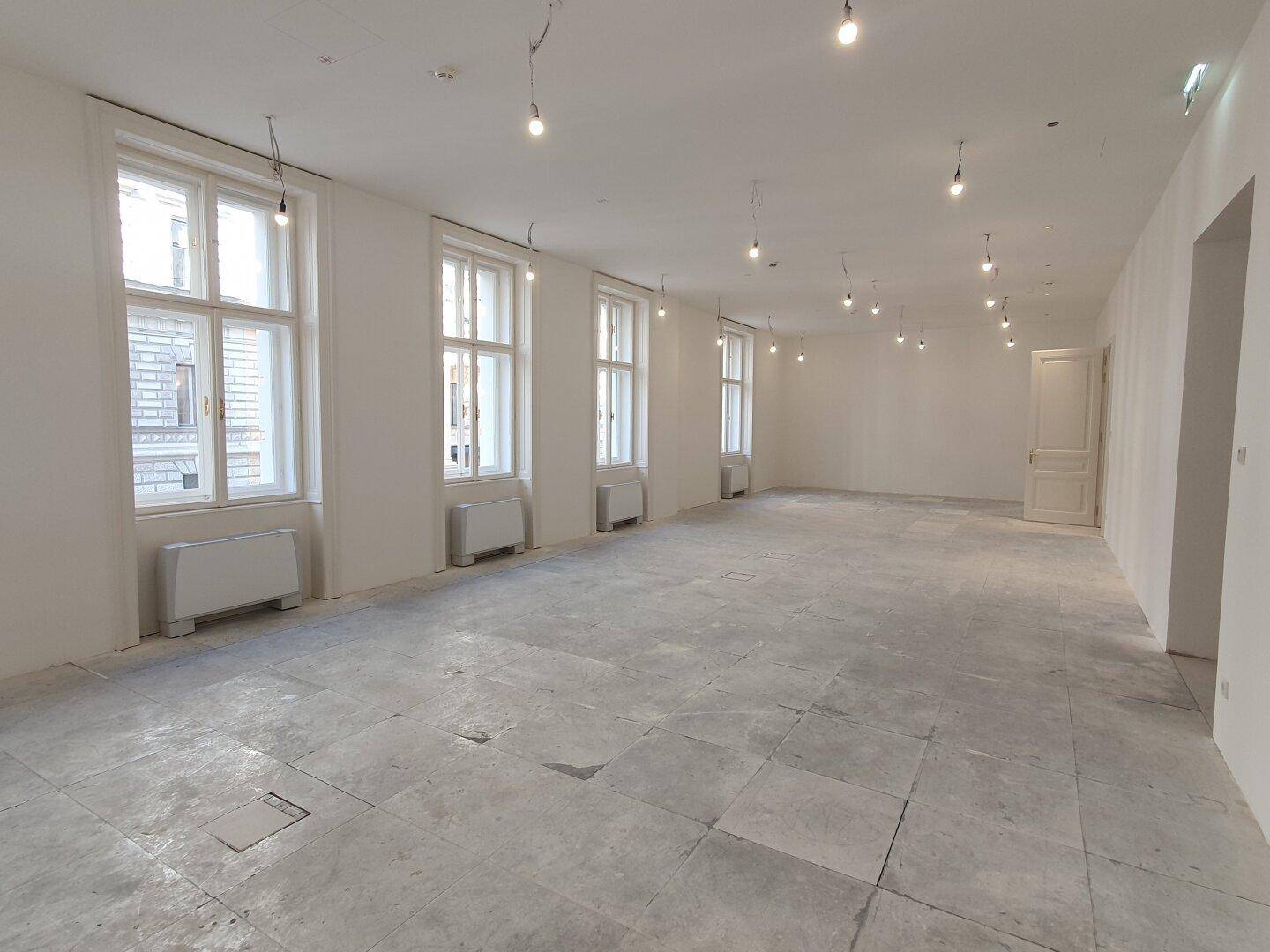 Geräumiger, heller Raum mit vielen Fenstern und Betonboden, bereit für den Innenausbau.