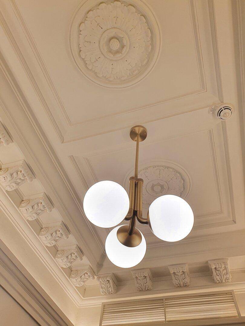 Elegante Decke mit Stuckverzierungen und einem modernen Kronleuchter mit drei Kugeln.