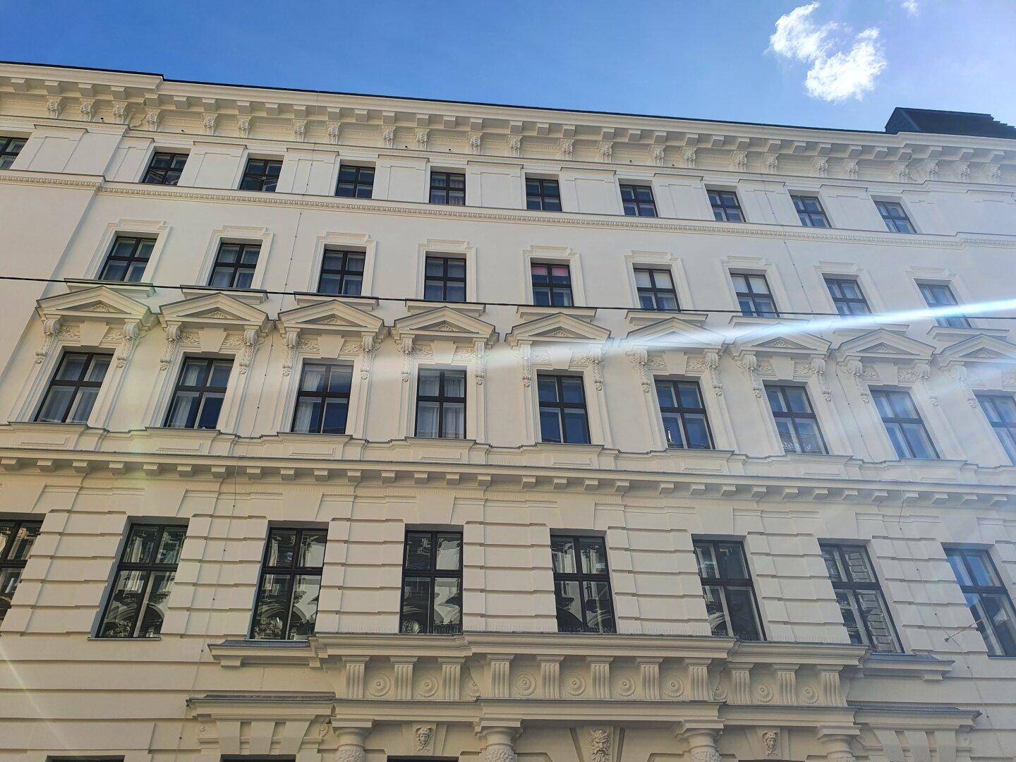 Klassische Gebäudefassade mit vielen Fenstern und dekorativen architektonischen Elementen unter blauem Himmel.