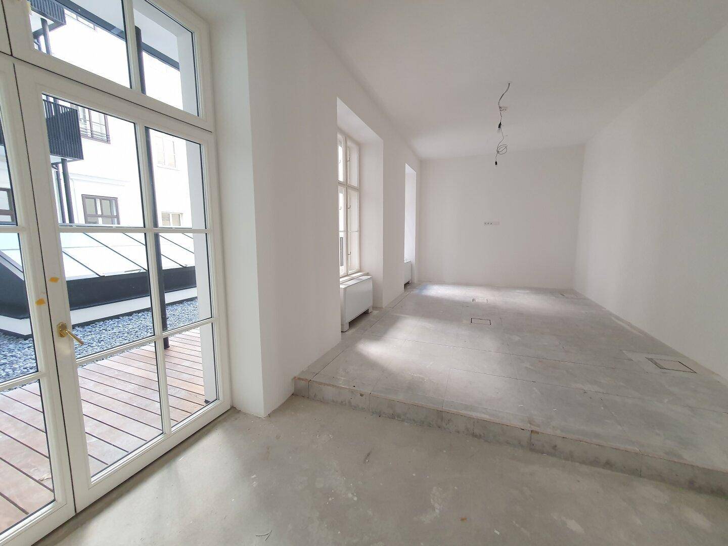 Heller Büroraum mit großer Glastür, die zu einer Außenterrasse mit Holzboden und Kies führt.