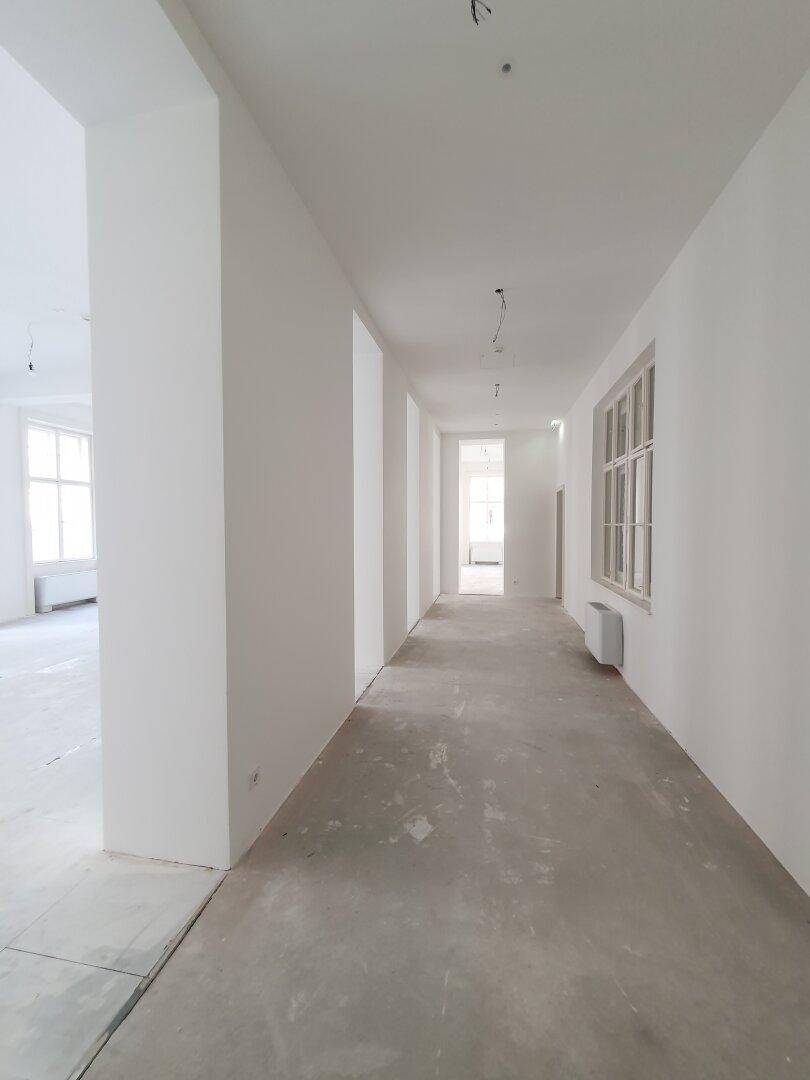 Langer, heller Flur mit weißen Wänden und einem Fenster am Ende, verbindet verschiedene Bürobereiche.