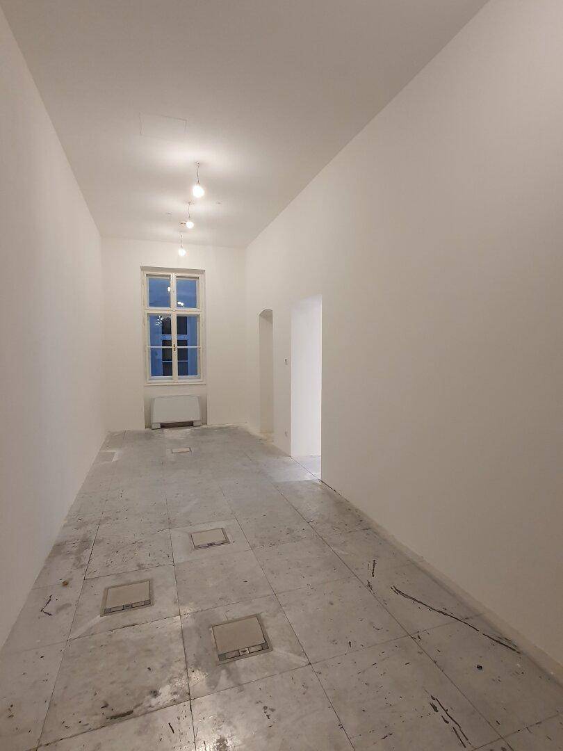 Langer, schmaler Raum mit einem Fenster und Betonboden, ideal für einen Flur oder Abstellraum.