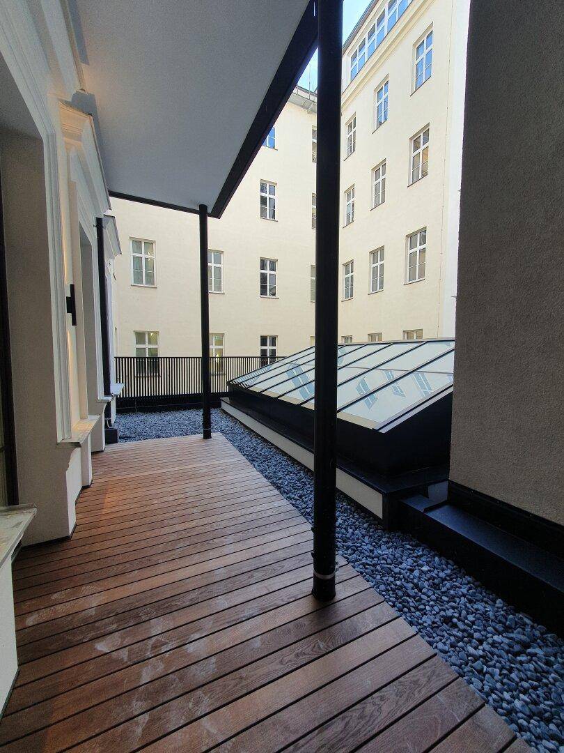 Moderne Terrasse mit Holzdeck und Kiesbett, umgeben von Gebäuden und einem Oberlicht.