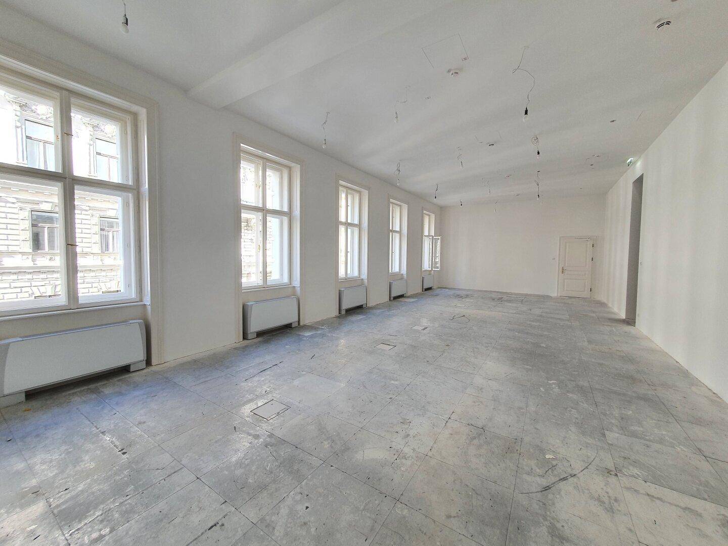 Geräumiger Bürobereich mit vielen Fenstern, weißen Wänden und einem robusten Betonboden.