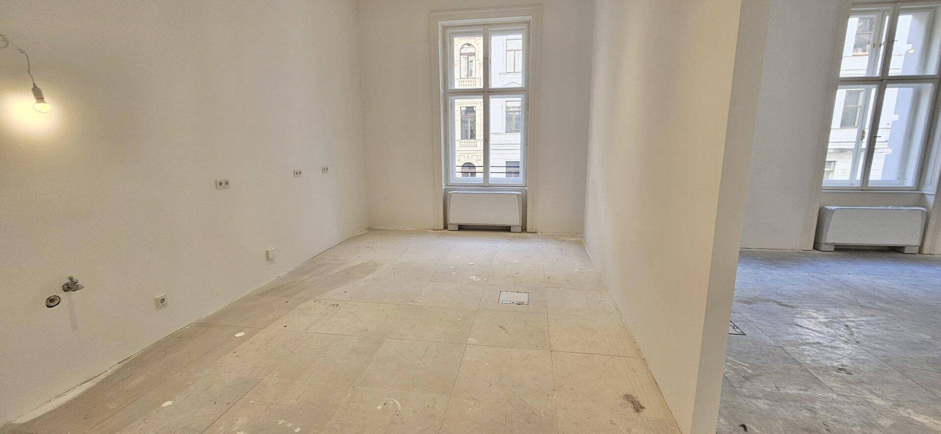 Kleinerer Büroraum mit einem Fenster und sichtbaren Anschlüssen für Installationen, im Rohbauzustand.
