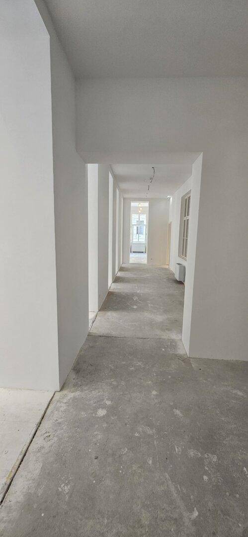 Langer, heller Flur mit weißen Wänden und einem Fenster am Ende, der zu weiteren Räumen führt.
