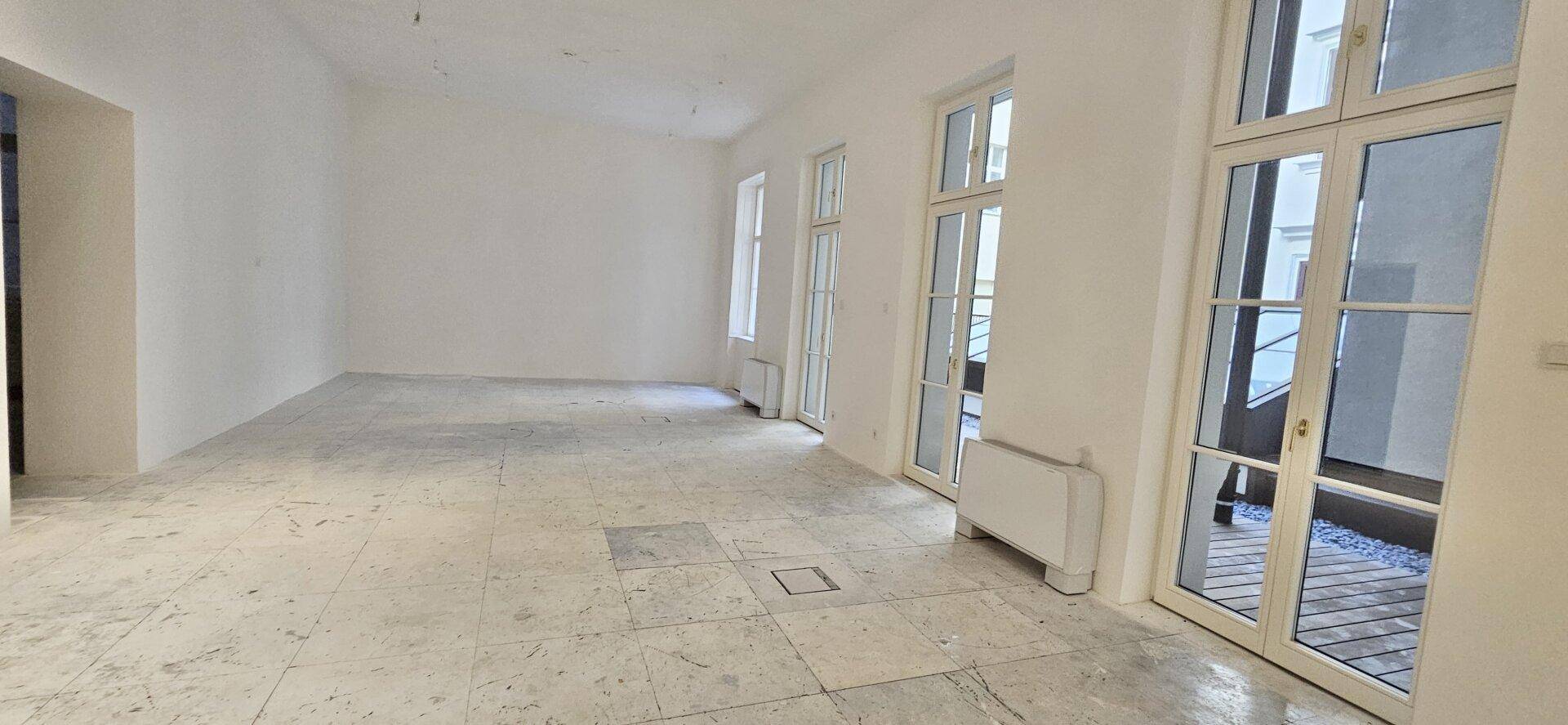 Heller Büroraum im Rohbau mit Zugang zu einem Außenbereich und Betonboden, bereit für den Ausbau.