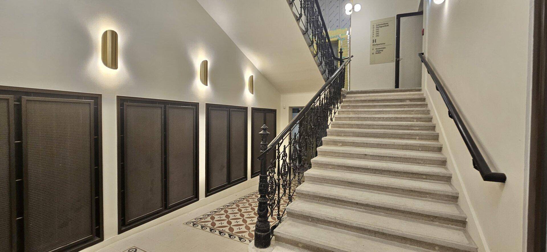 Elegantes Treppenhaus mit Steinstufen, schmiedeeisernem Geländer und dekorativen Wandleuchten.