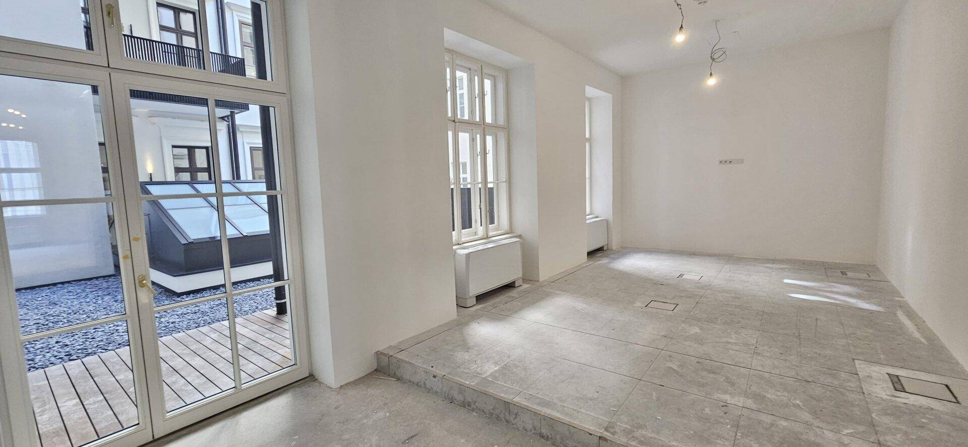 Heller Büroraum im Rohbau mit Zugang zu einem Außenbereich und Betonboden, bereit für den Ausbau.