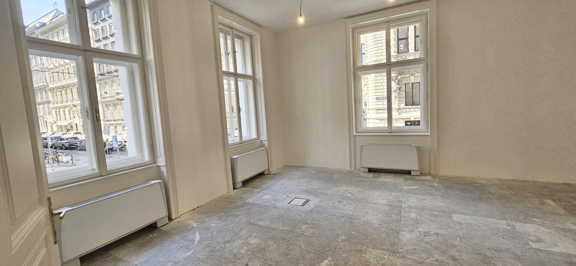Heller Büroraum im Rohbau mit zwei großen Fenstern und Betonboden, bereit für die Gestaltung.