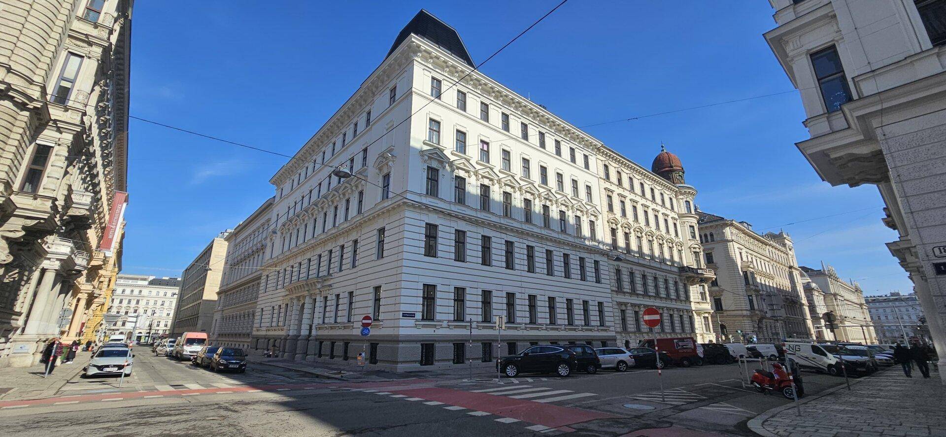Historisches Gebäude mit klassischer Architektur und vielen Fenstern an einer belebten Straße.