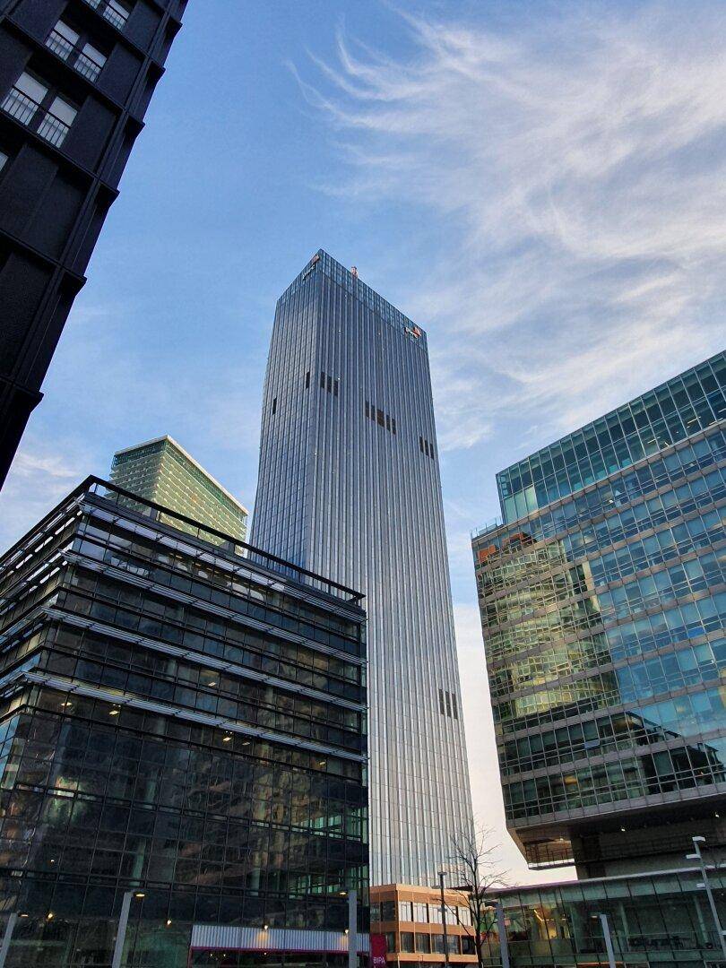 Markanter, hoher Wolkenkratzer mit gerippter Fassade, umgeben von modernen Glasgebäuden in der Stadt.