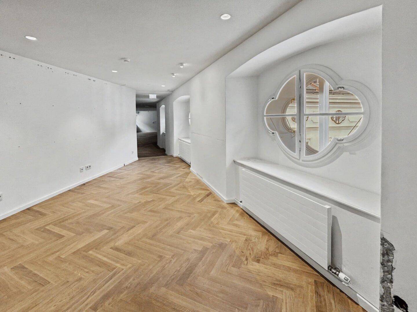Langer Flur oder Bürobereich mit Fischgrätparkett und einem markanten Rundbogenfenster, das Licht hereinlässt.