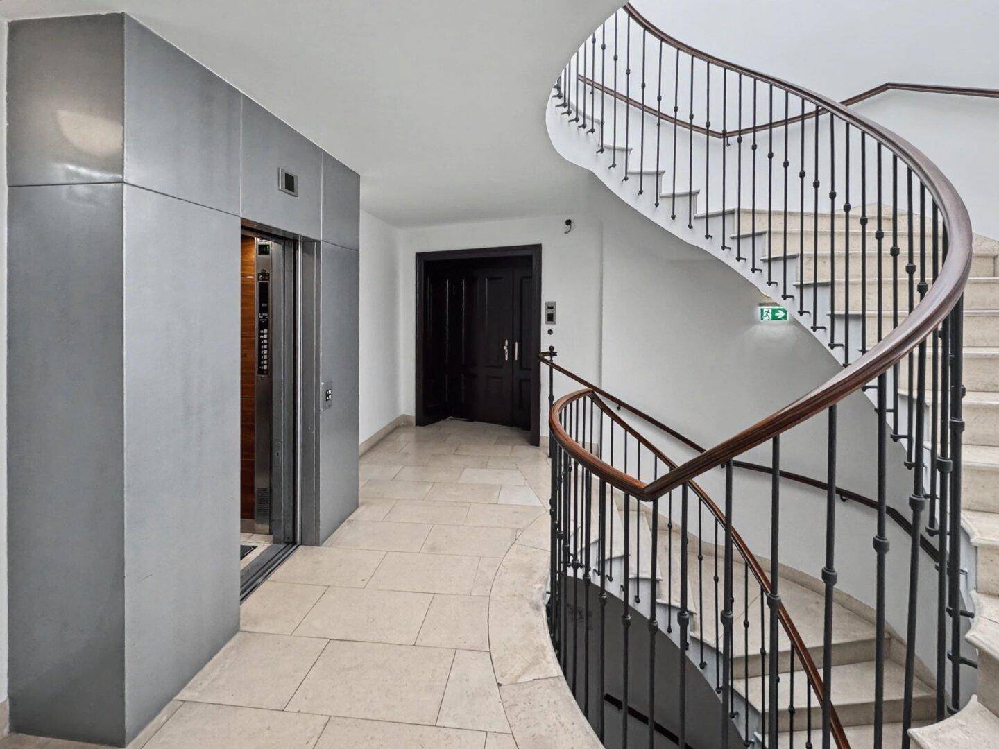 Heller Flur mit modernem Aufzug und eleganter Wendeltreppe, die zu den oberen Etagen führt.