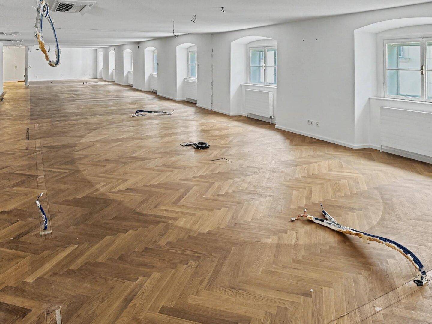 Großer, offener Bürobereich mit Fischgrätparkett und vielen Fenstern, die viel Tageslicht hereinlassen.