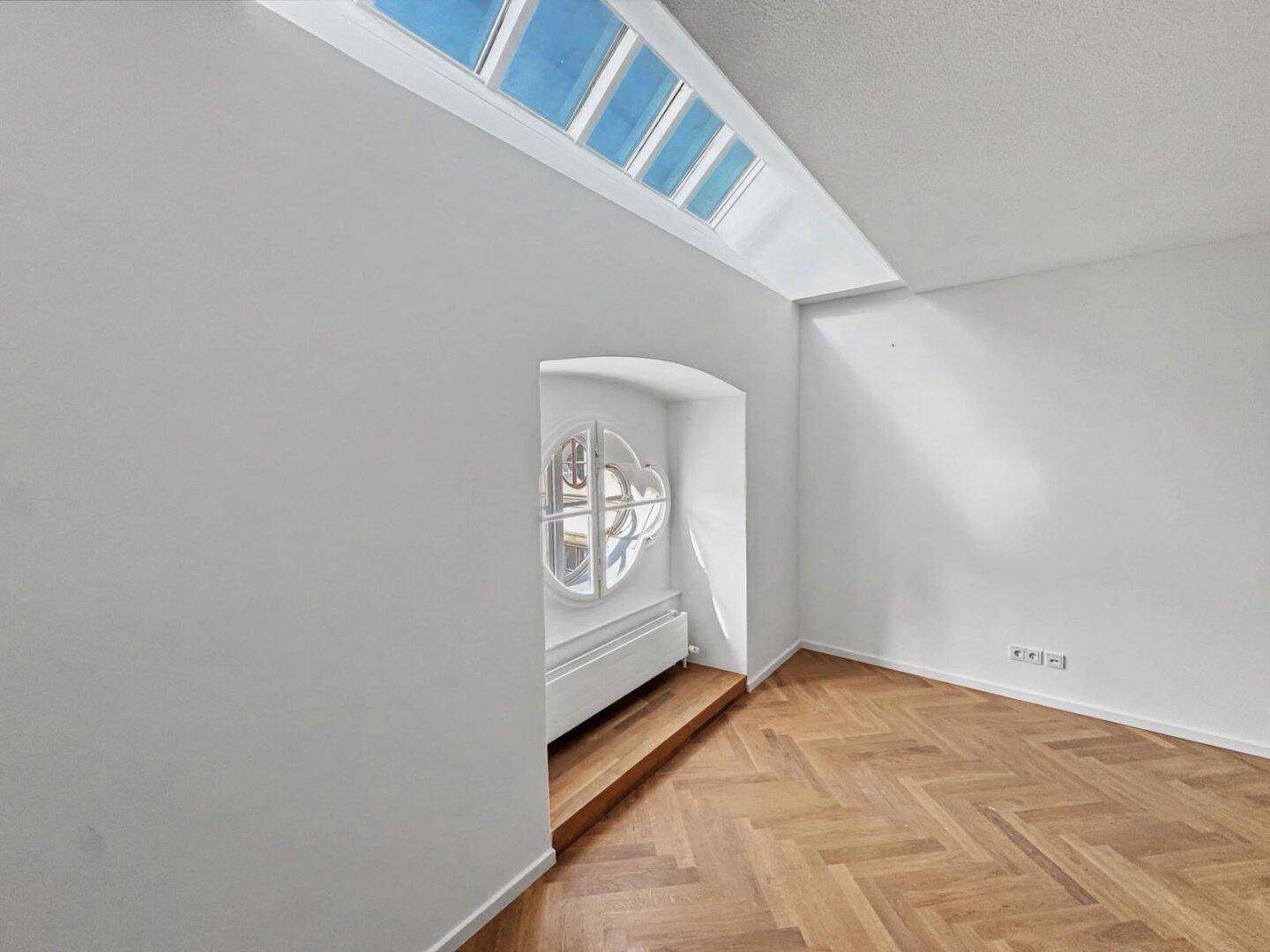 Heller Büroraum mit Fischgrätparkett, Oberlichtern und einem dekorativen Rundbogenfenster, das viel Licht spendet.