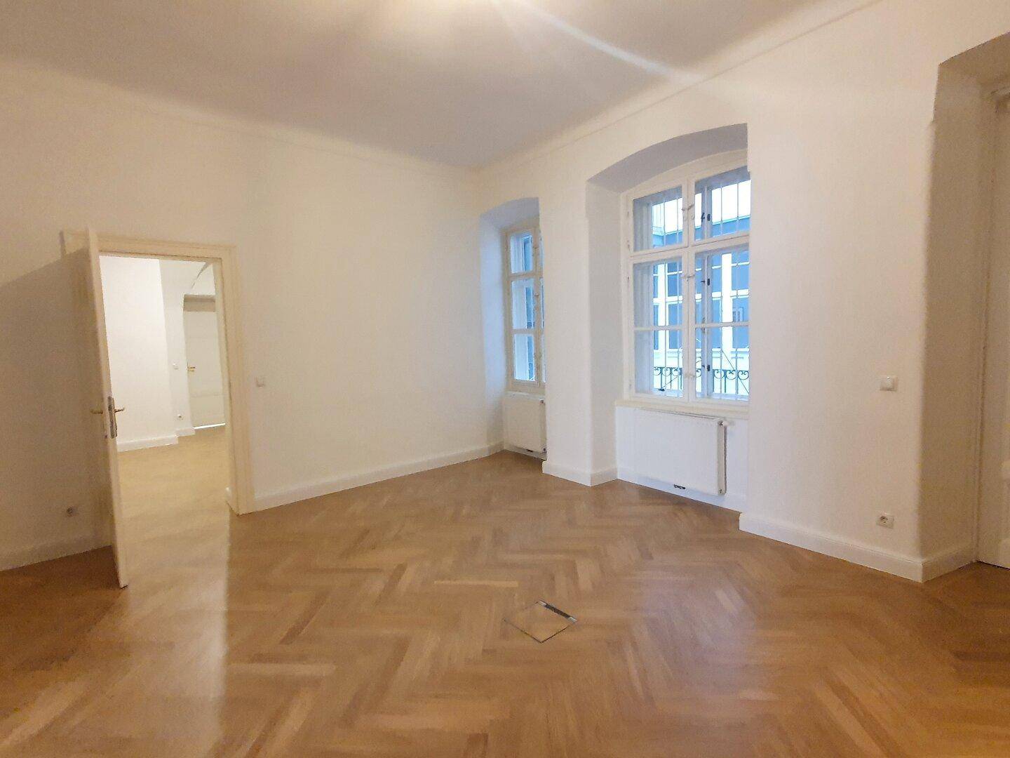 Heller Raum mit Fischgrätparkett und einem großen Fenster, das viel Tageslicht hereinlässt.