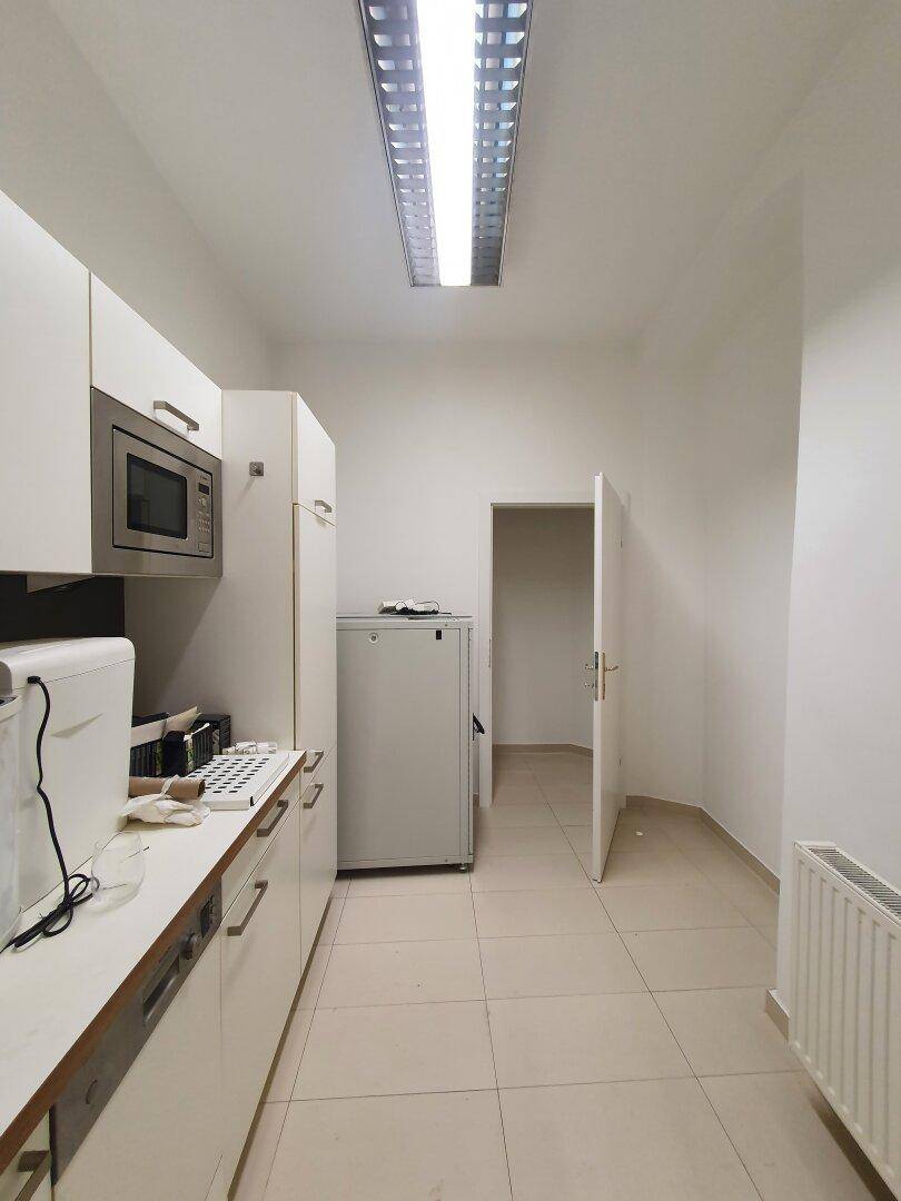 Funktionale Teeküche mit weißen Schränken, Mikrowelle und Kühlschrank, ideal für kleine Pausen.