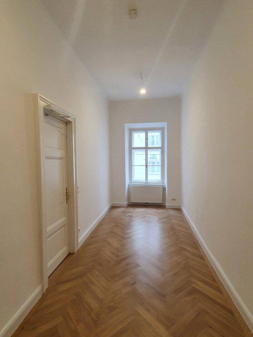 Schmaler Raum mit Fischgrätparkett und einem Fenster, das für Tageslicht sorgt.