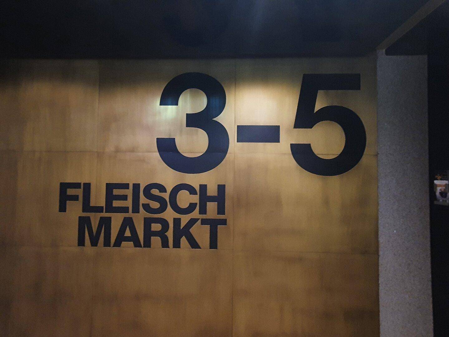 Detailansicht der Beschilderung "Fleisch Markt 3-5" an einer goldenen Wand.