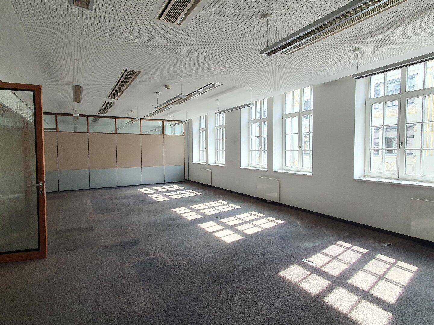Geräumiges Büro mit Teppichboden, vielen Fenstern und Trennwänden.