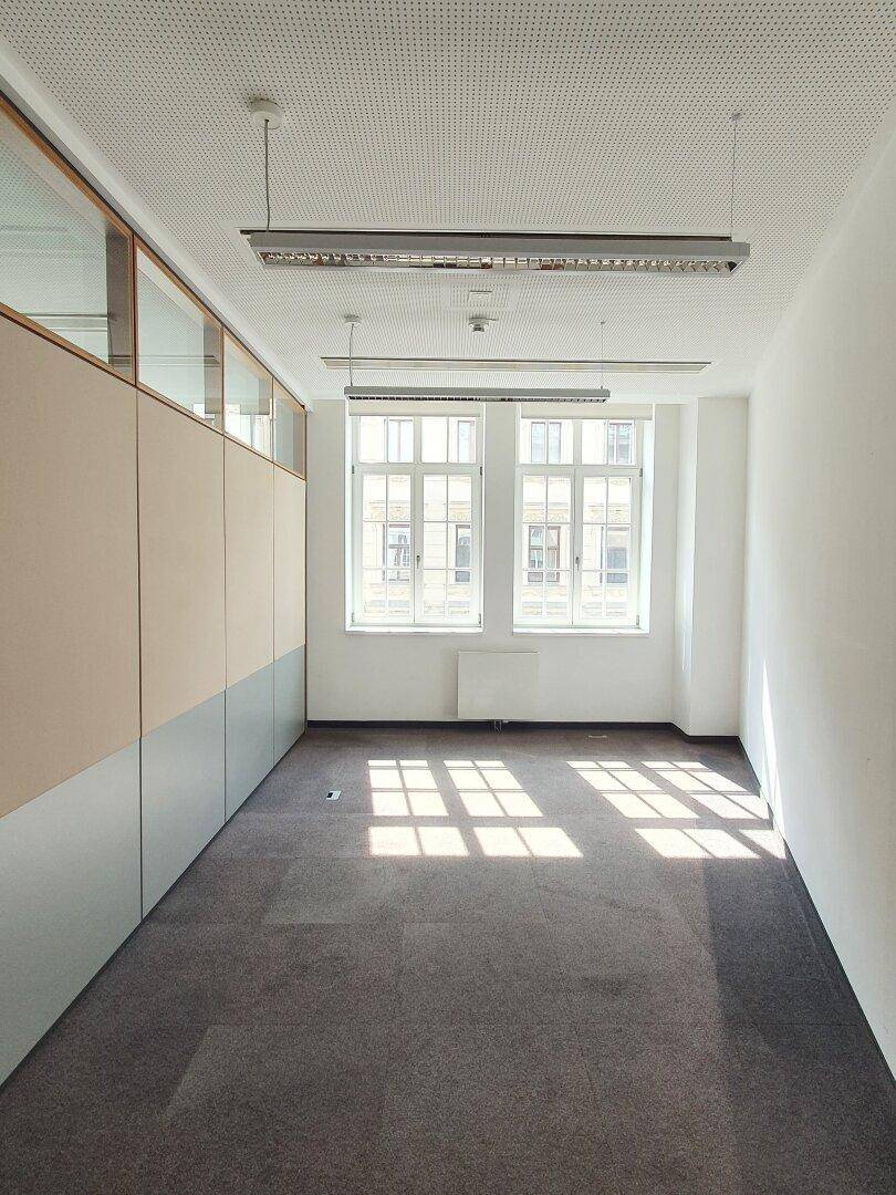 Kleineres Büro mit Teppichboden, einem Fenster und Trennwänden.