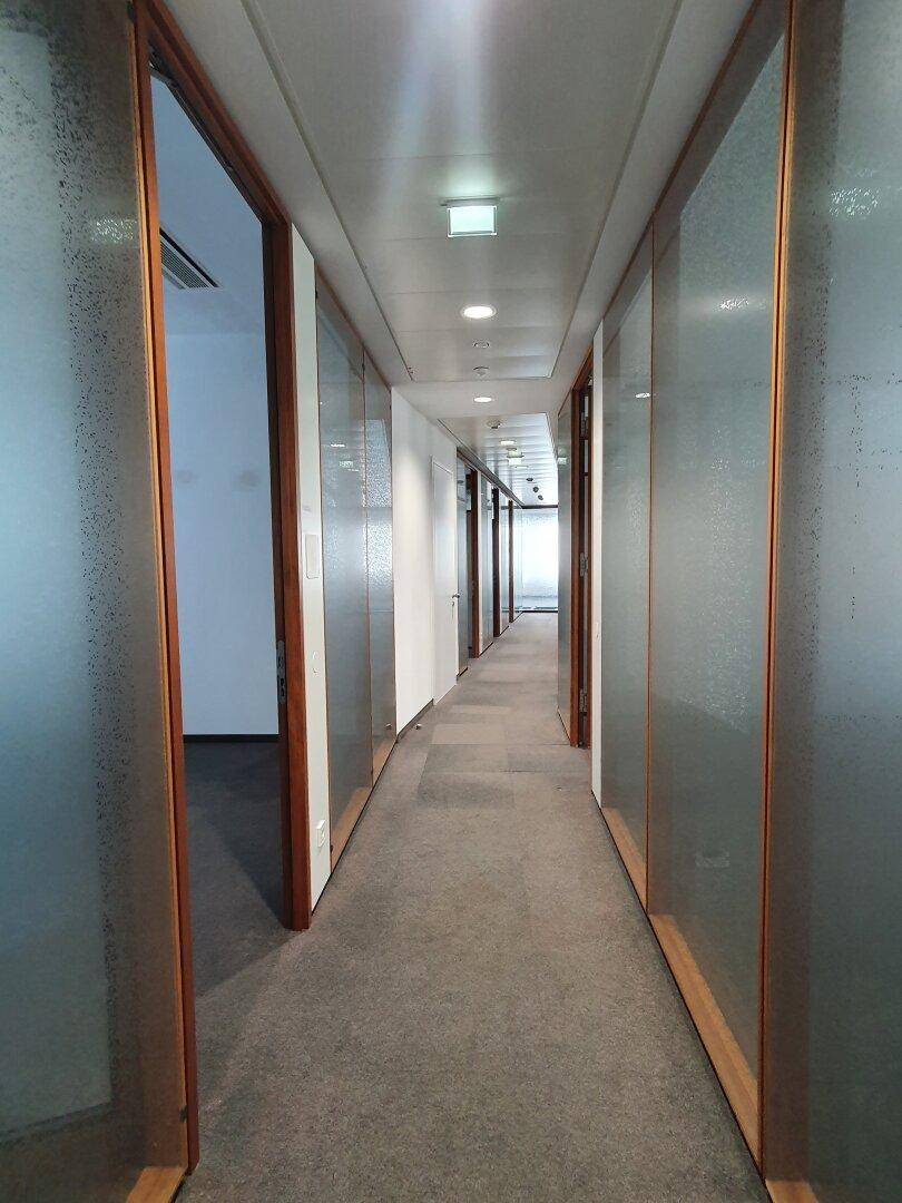 Langer Flur mit Glaswänden und Holzelementen, der zu Büroräumen führt.