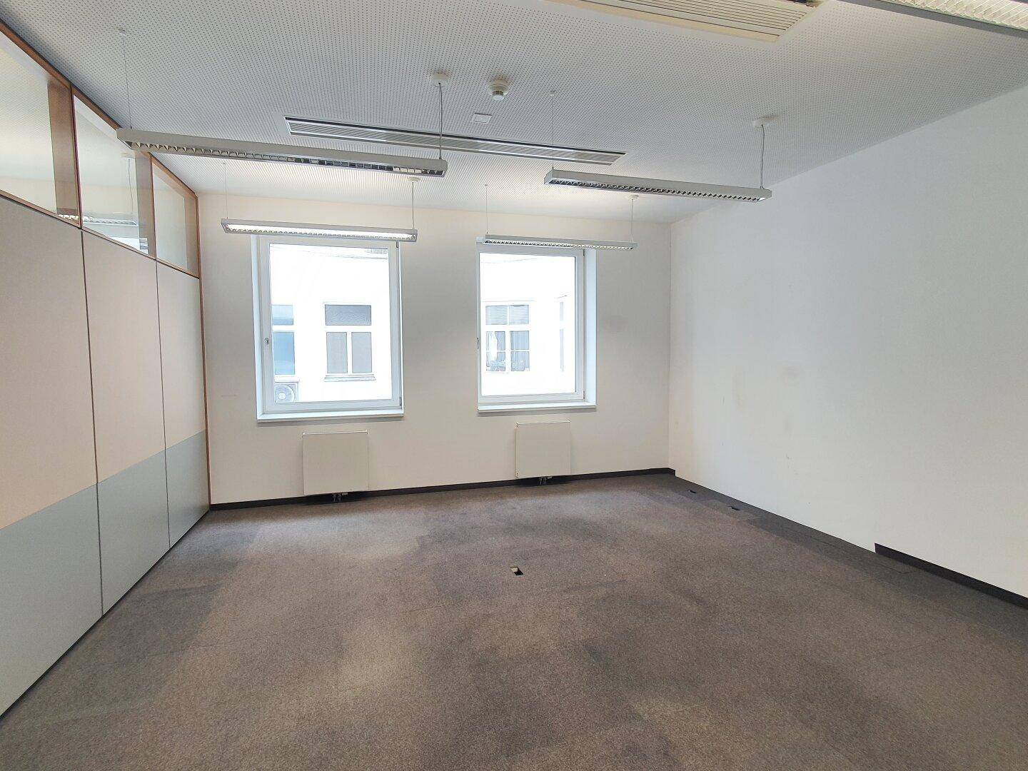 Büro mit Teppichboden, zwei Fenstern und Trennwänden.