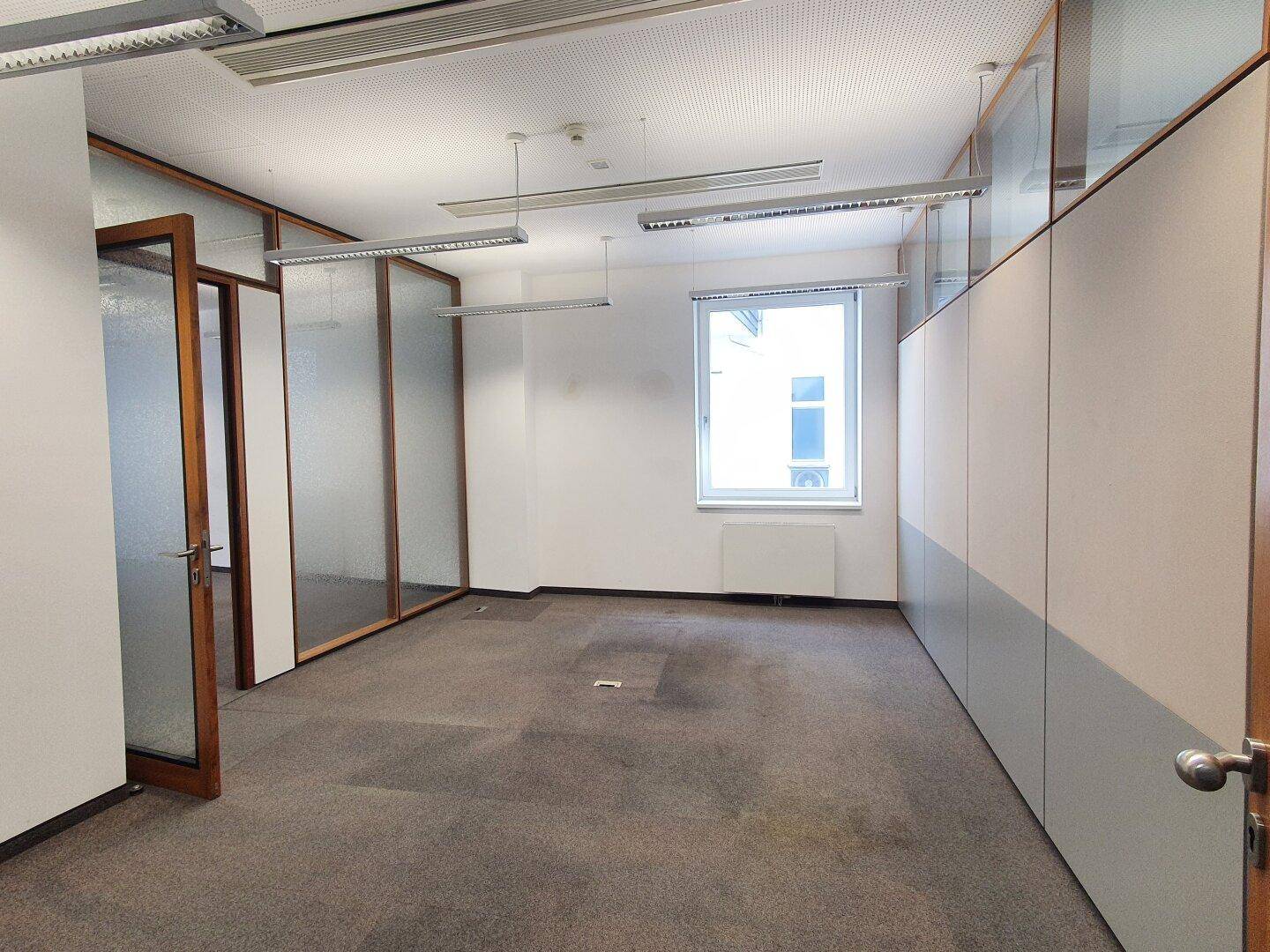Büro mit Teppichboden, einem Fenster und Trennwänden mit Glas.