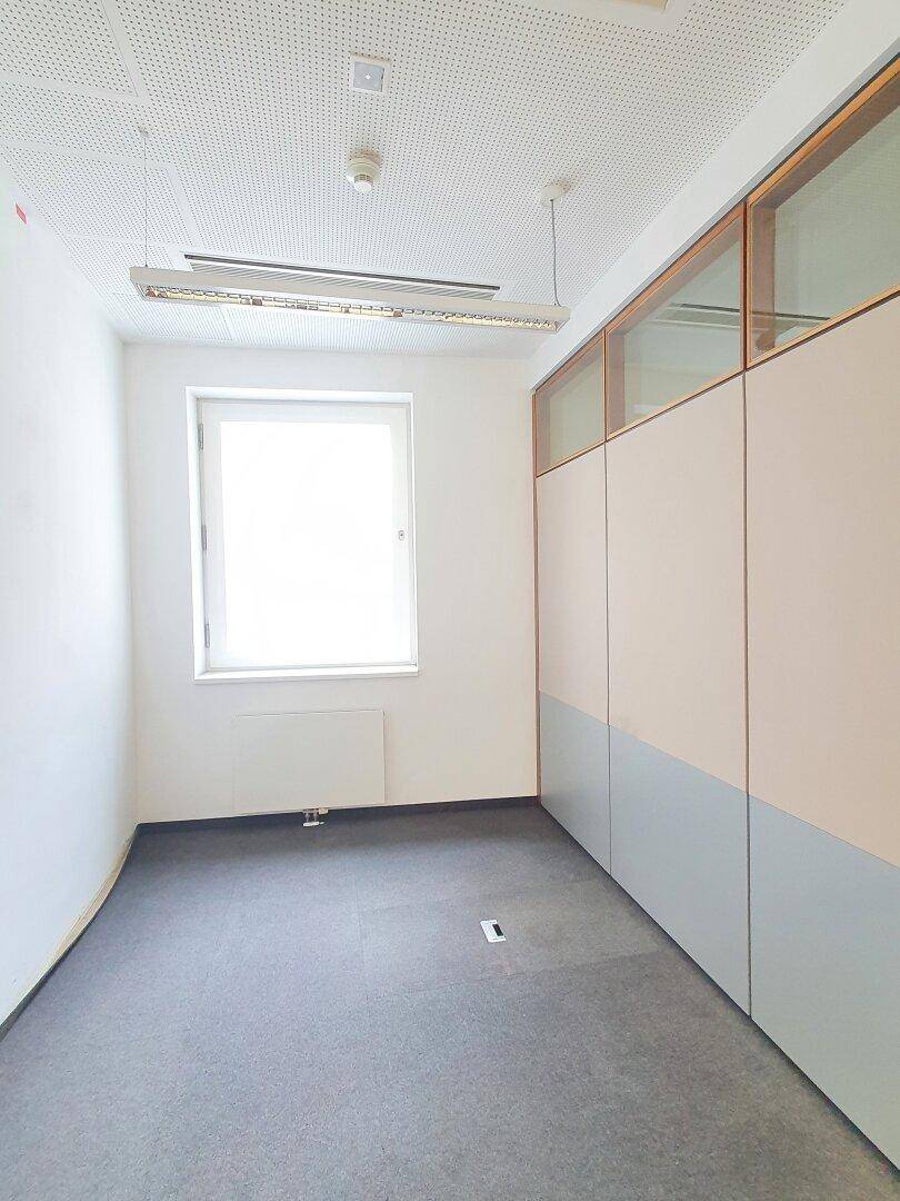 Kleineres Büro mit Teppichboden, einem Fenster und Trennwänden.