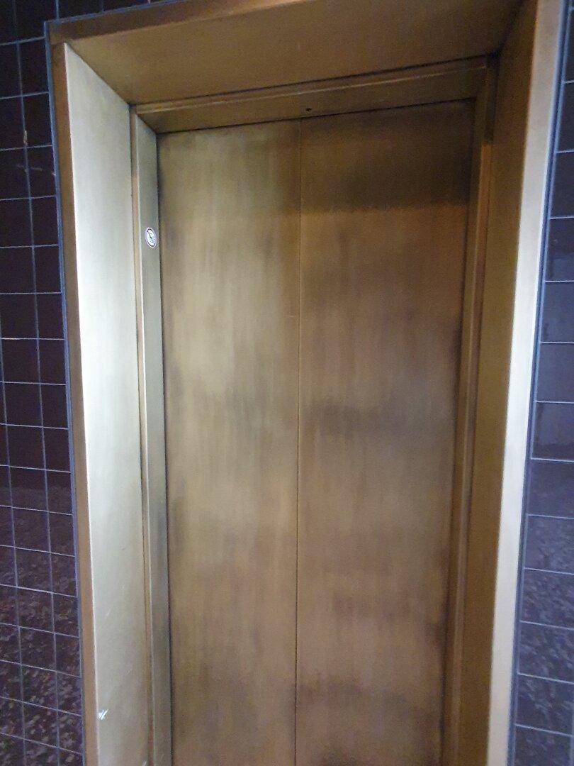 Detailansicht einer goldenen Aufzugstür in einem gefliesten Bereich.