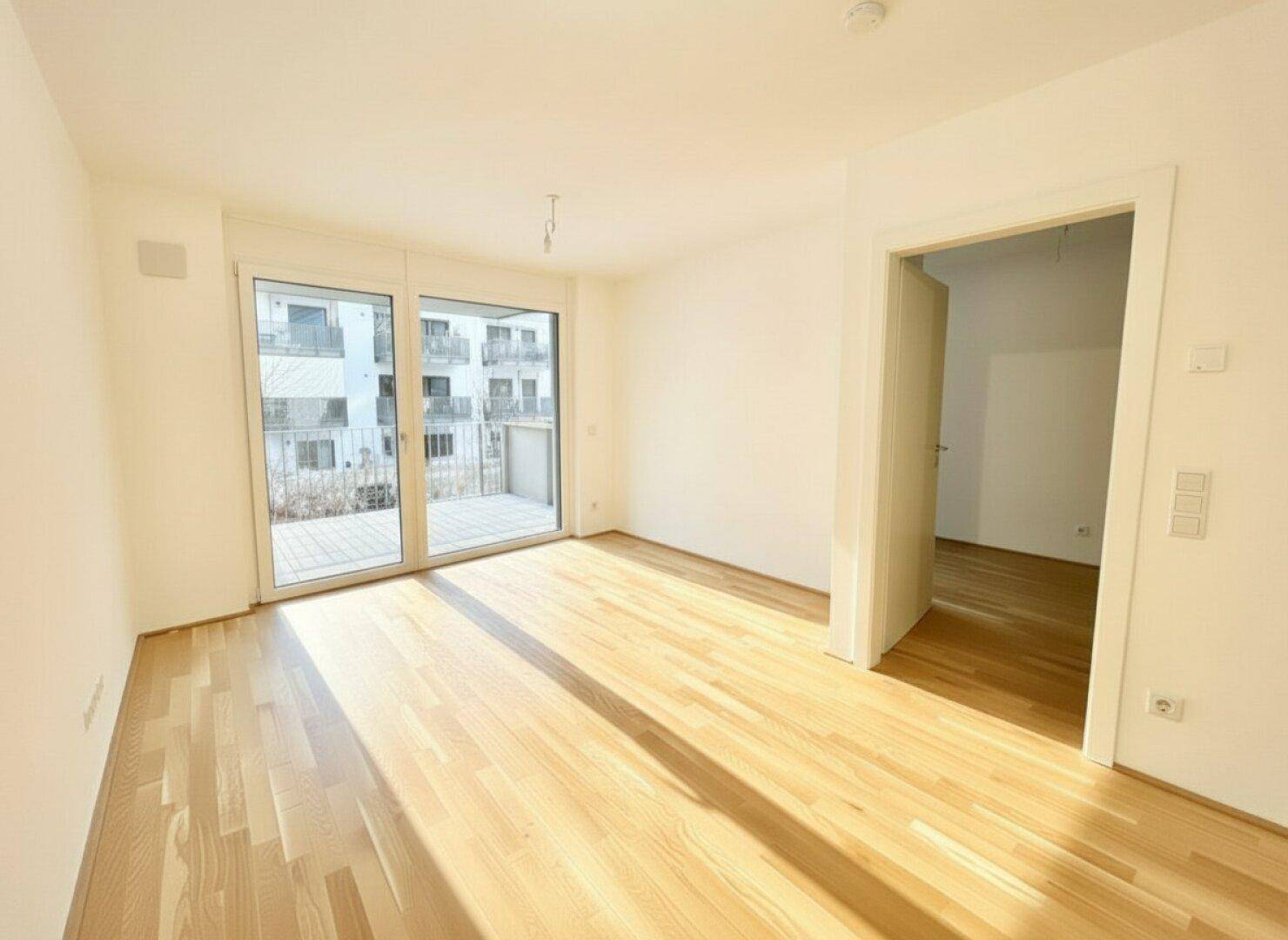 Heller Wohnbereich mit Parkettboden und großen Fenstern, die auf einen Balkon führen.
