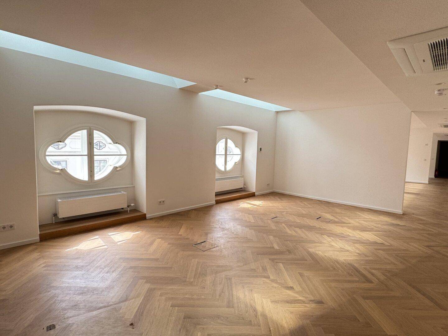 Großer, heller Büroraum mit Fischgrätparkett und dekorativen Rundfenstern.