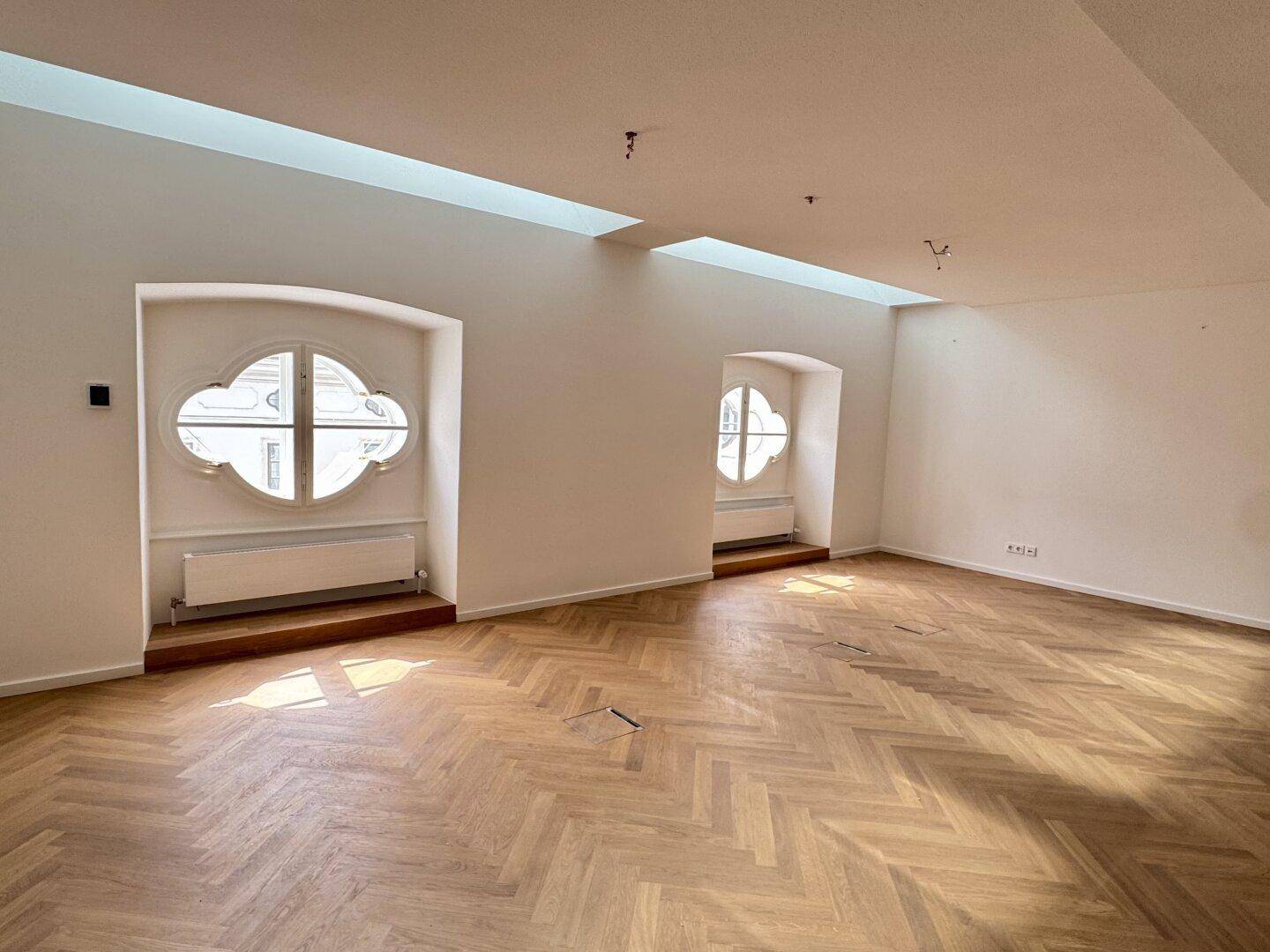 Geräumiger Bürobereich mit Fischgrätparkett und zwei eleganten Rundfenstern.
