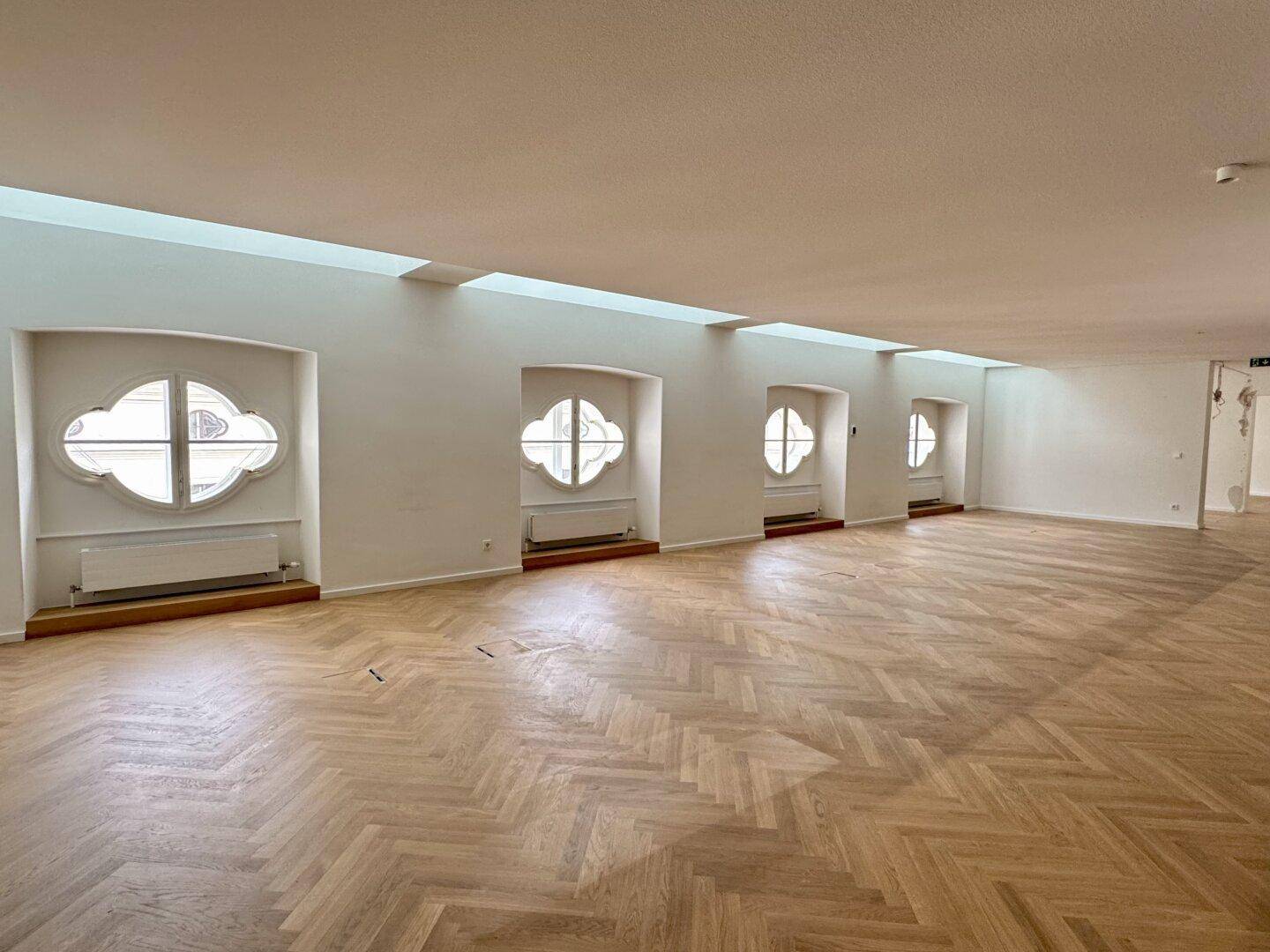 Großer, heller Büroraum mit Fischgrätparkett und einer Reihe von Rundfenstern.