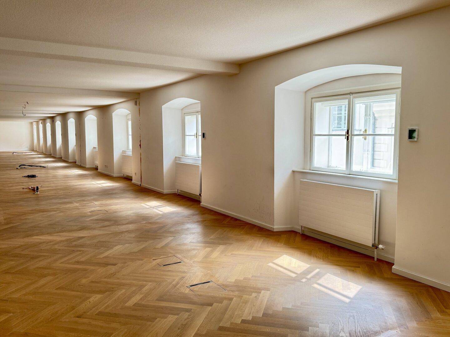 Heller Flur mit Fischgrätparkett und Fenstern, die natürliches Licht hereinlassen.