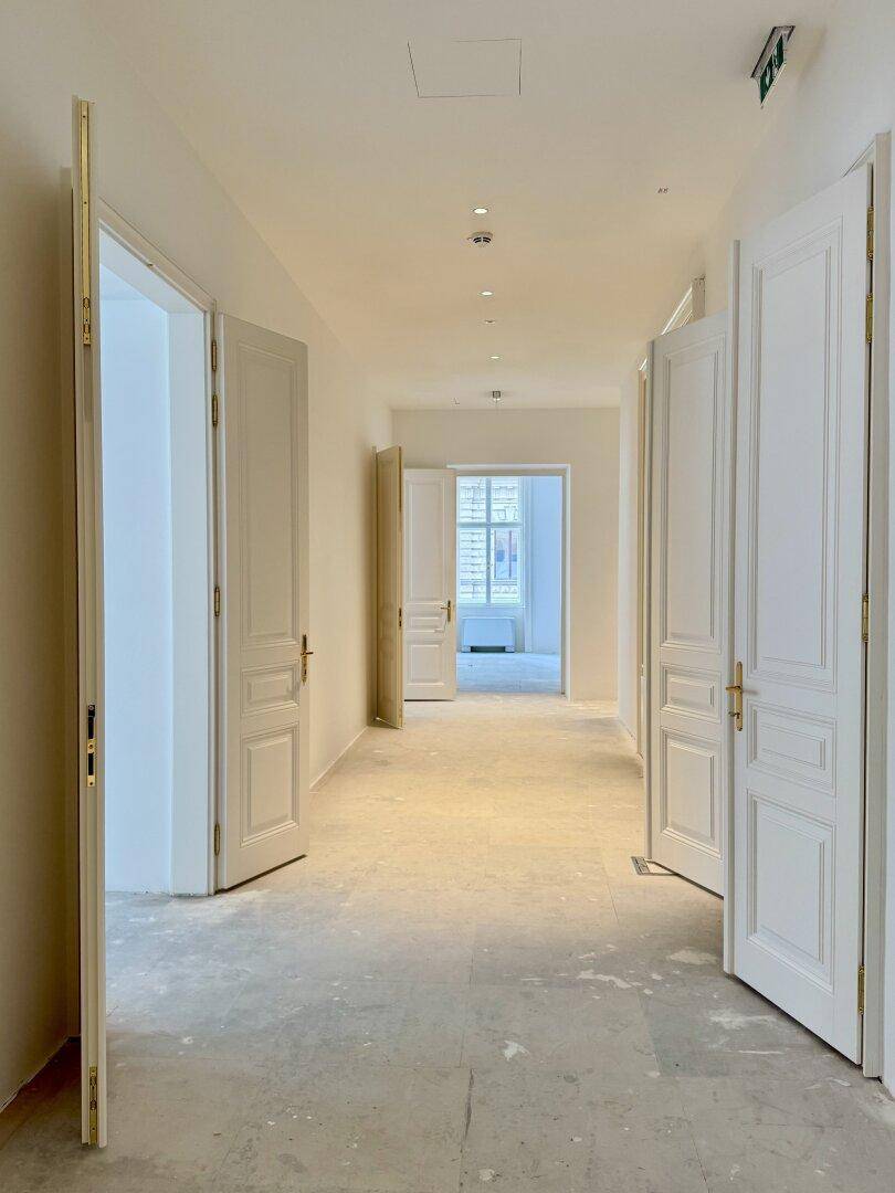 Heller Flur mit mehreren geöffneten Türen und Einbaustrahlern an der Decke.