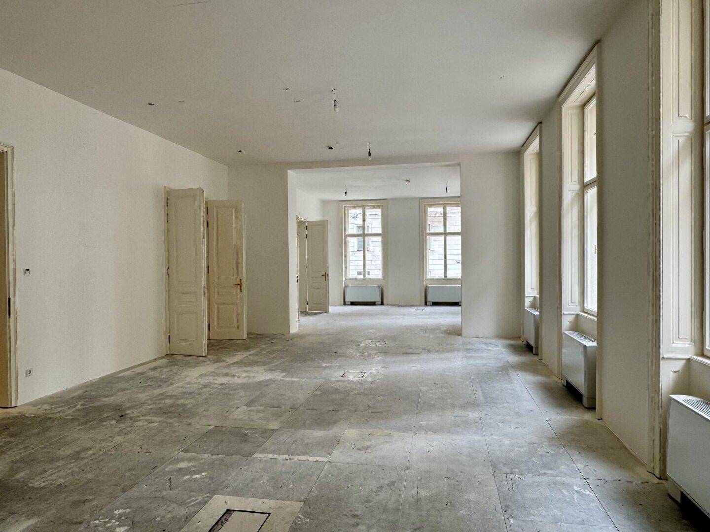 Geräumiger, leerer Raum mit hohen Fenstern und Fliesenboden, ideal für Büronutzung.