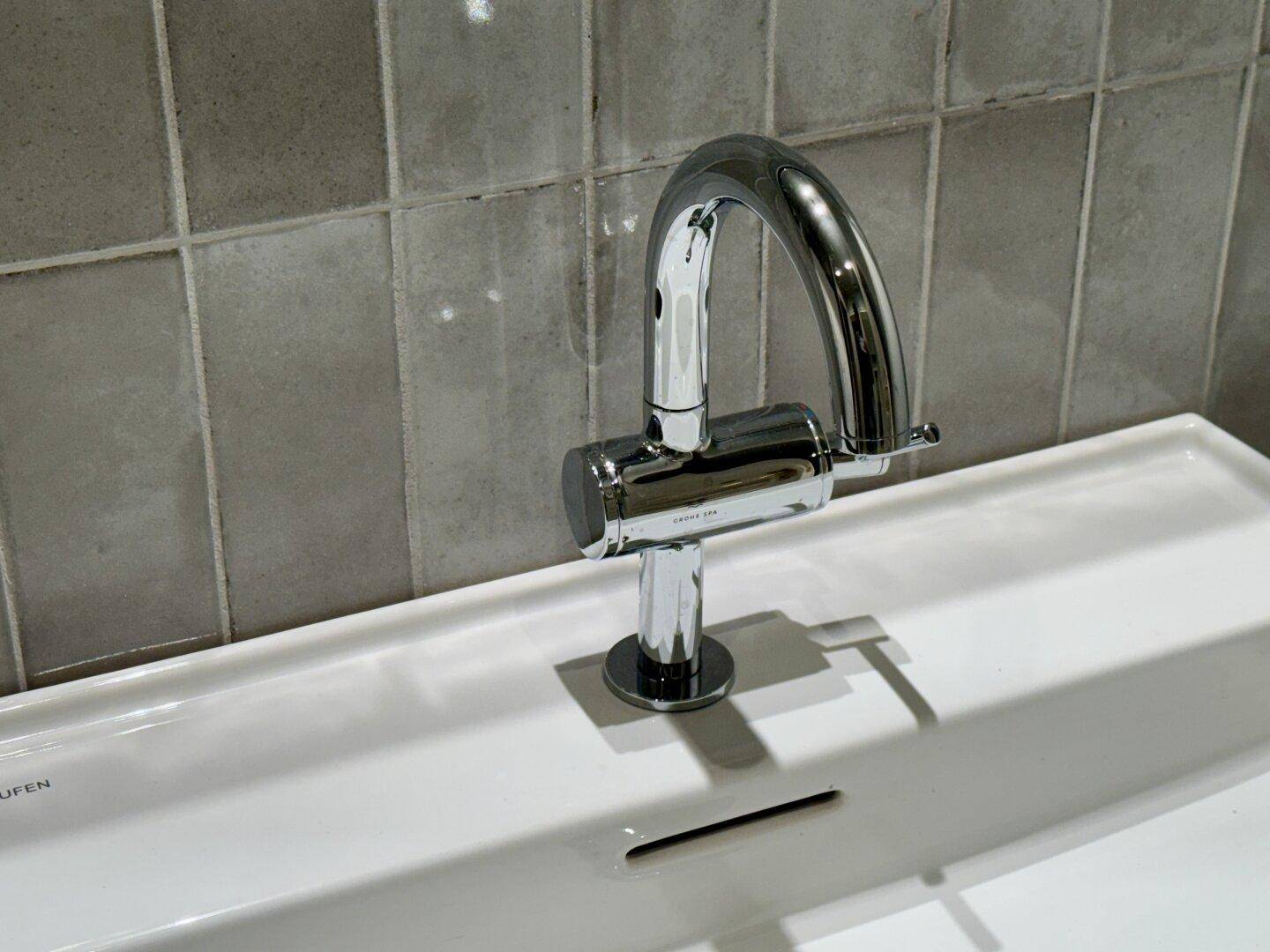Detailansicht eines modernen Wasserhahns über einem weißen Waschbecken.