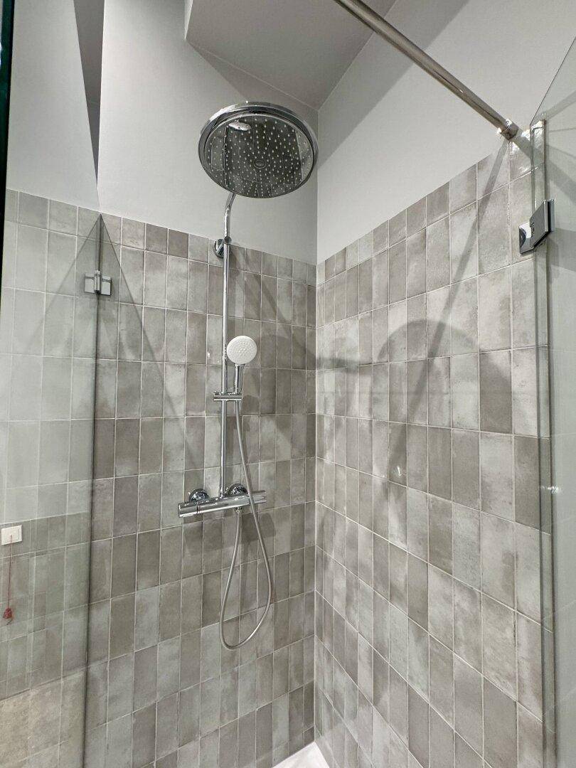 Ebenerdige Dusche mit Regenduschkopf und modernen grauen Fliesen.