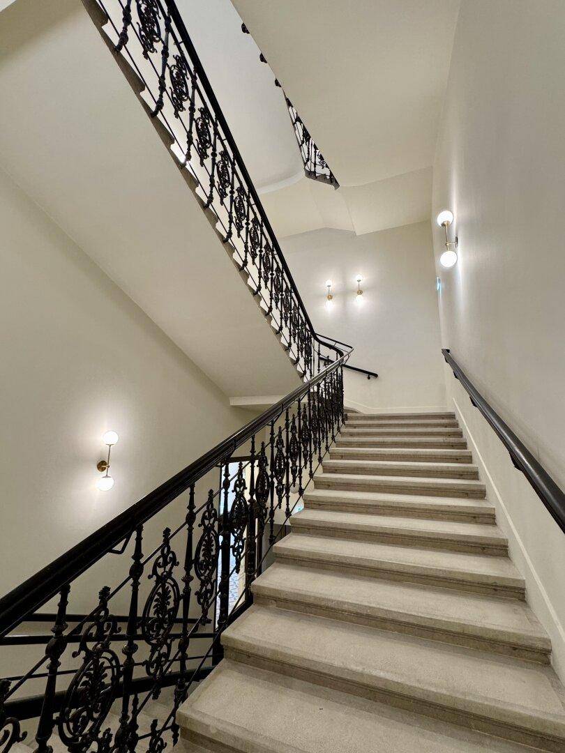 Elegantes Treppenhaus mit geschwungenem schmiedeeisernem Geländer und Stein-Stufen.