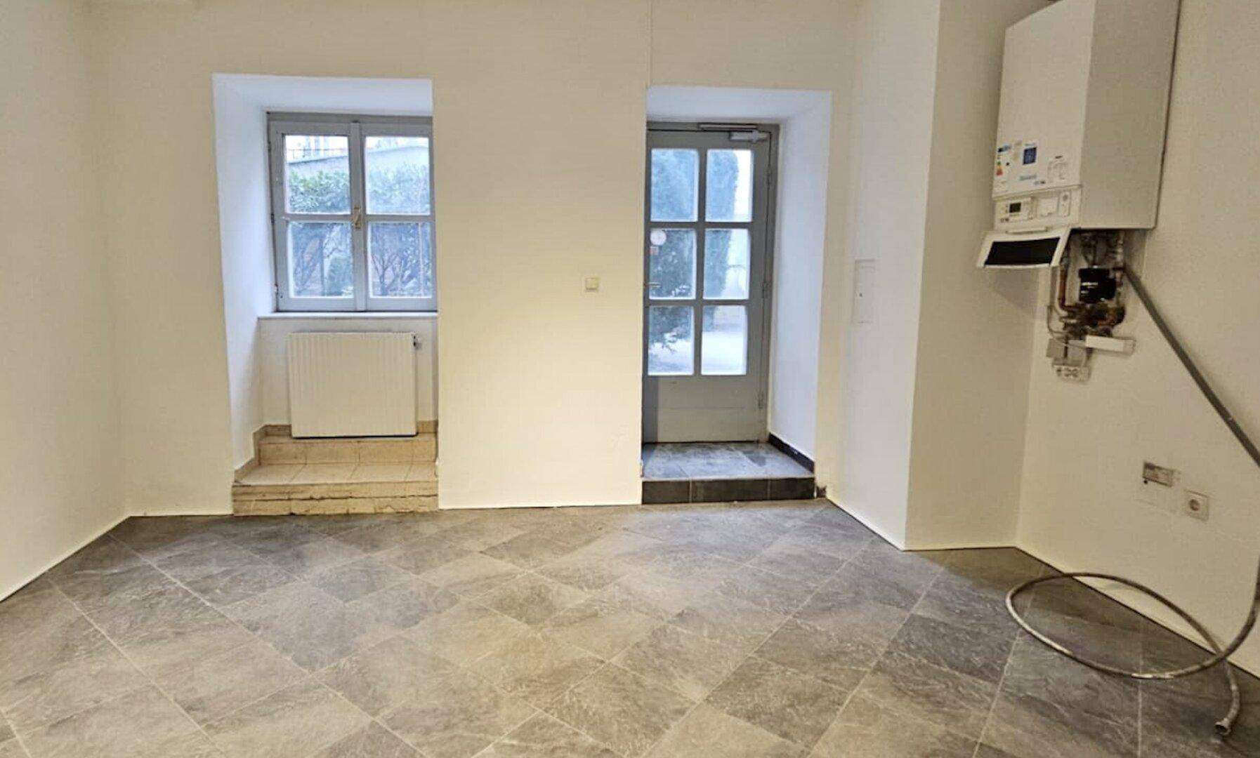 Leerer Raum mit Fliesenboden, einem Fenster, einer Tür und einem an der Wand montierten Warmwasserbereiter.