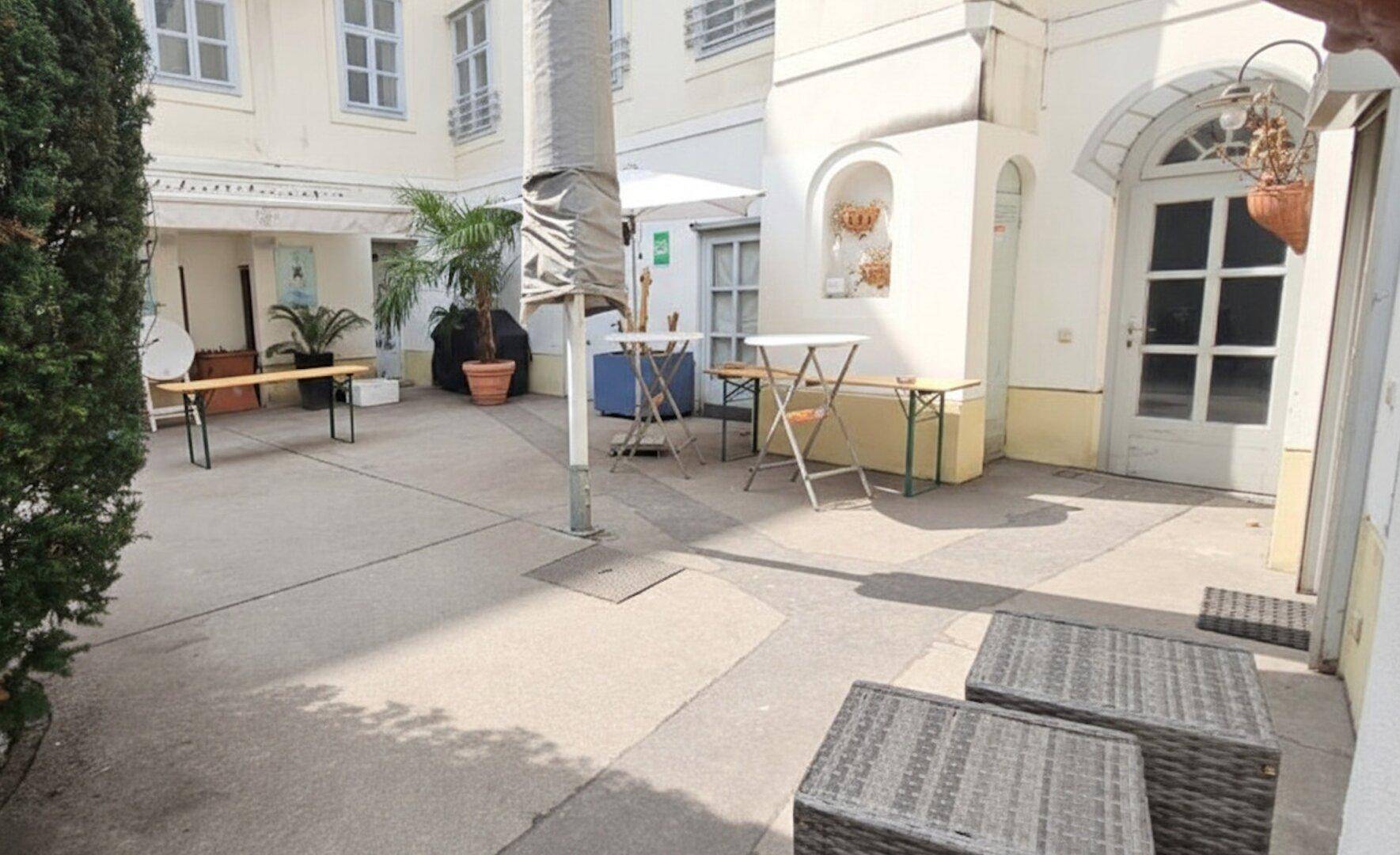 Gepflasterter Innenhof mit Sitzgelegenheiten, Pflanzen und historischen Gebäudefassaden, ideal für Pausen.