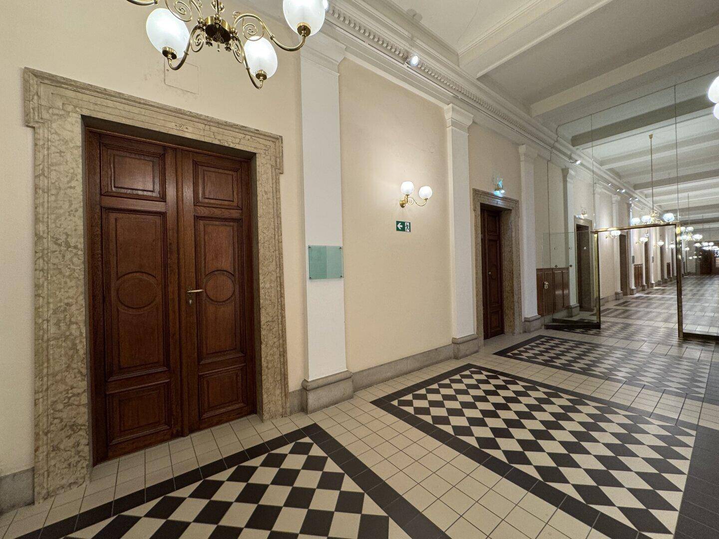Langer, eleganter Flur mit Schachbrettmuster-Fliesenboden, hohen Decken und mehreren Holztüren.