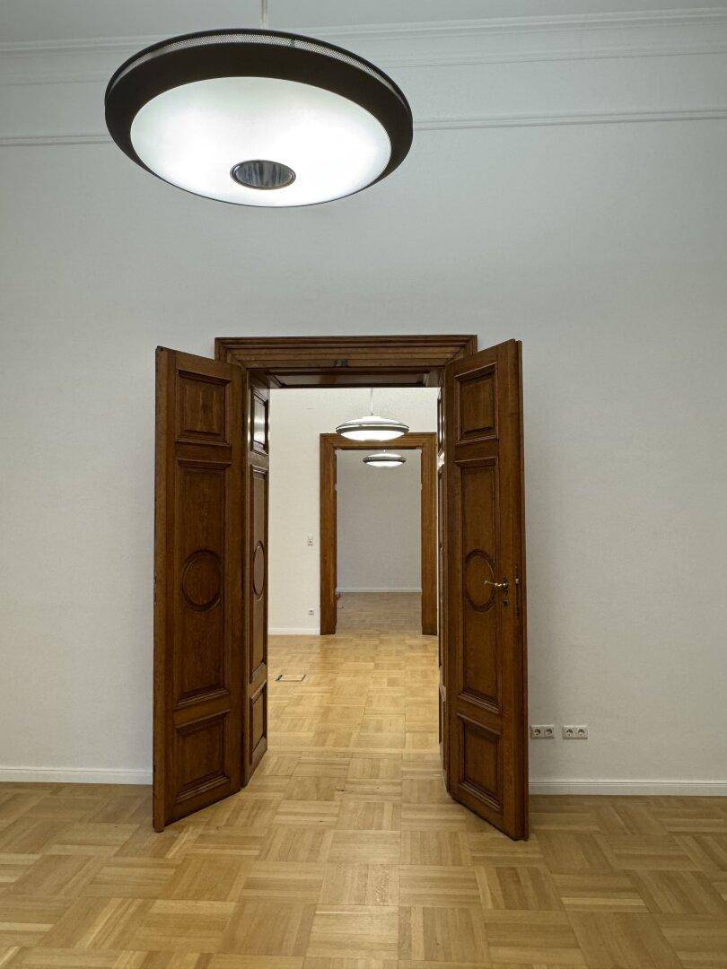 Blick durch eine Reihe offener Holztüren in aufeinanderfolgende, helle Räume mit Parkettboden.