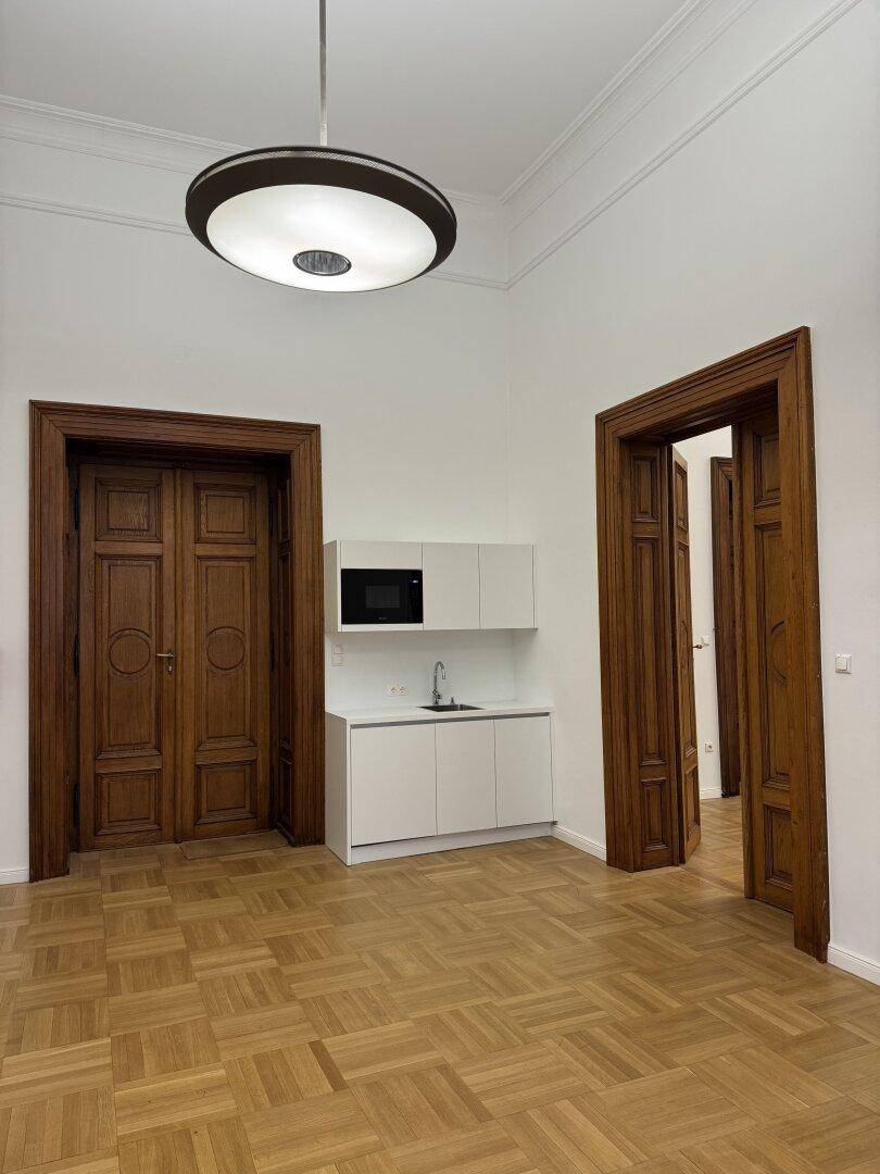 Heller Raum mit Parkettboden und einer modernen, weißen Küchenzeile, ideal für ein Büro.