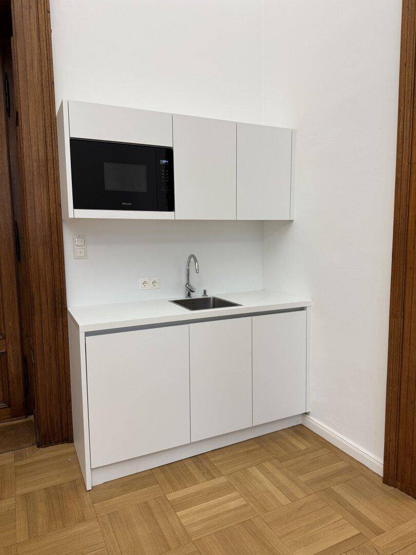 Moderne, weiße Küchenzeile mit Spüle und integrierter Mikrowelle, in einem hellen Raum.