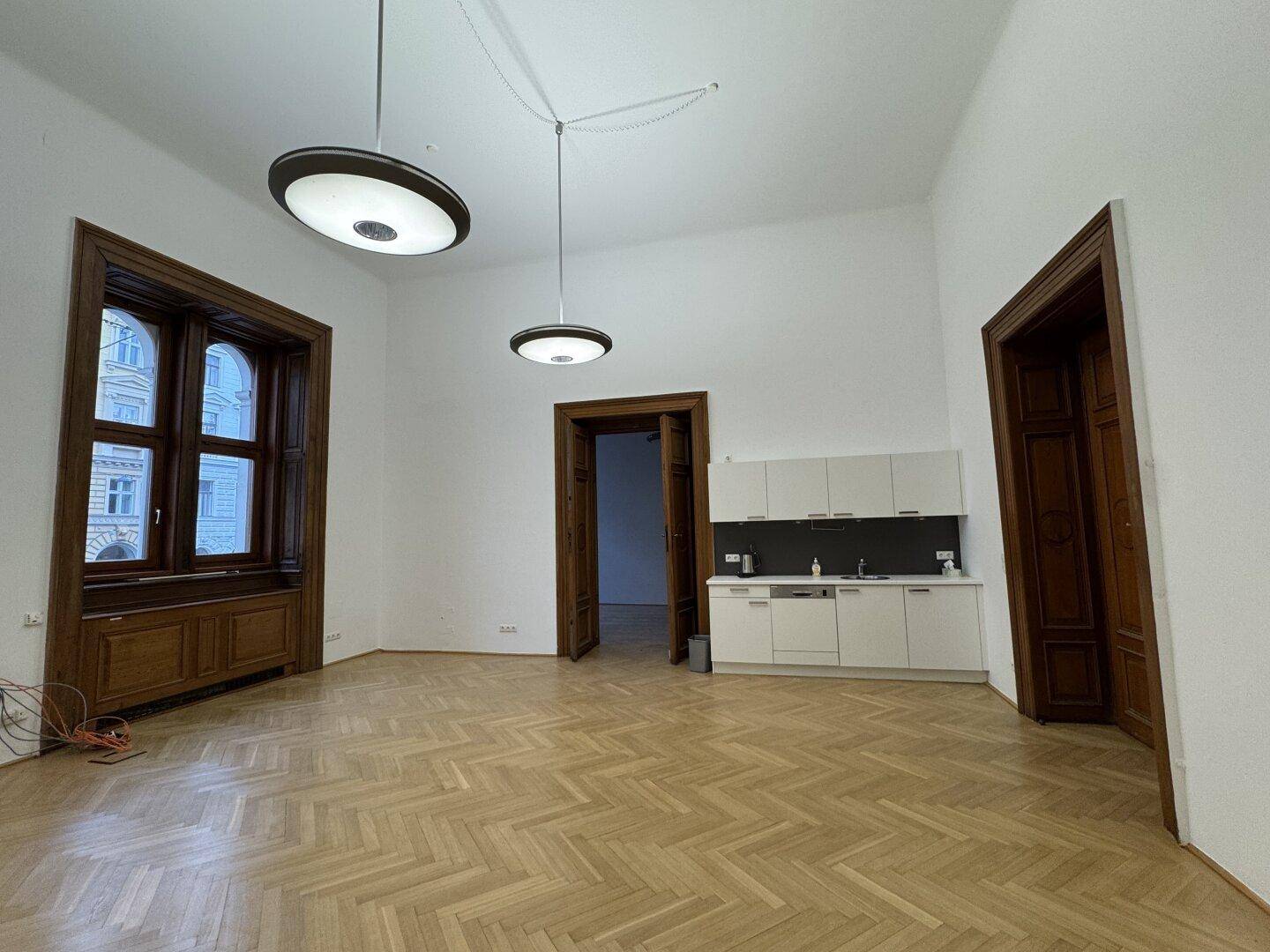 Heller Raum mit Fischgrätparkett, hohen Decken und einer integrierten, modernen Küchenzeile.