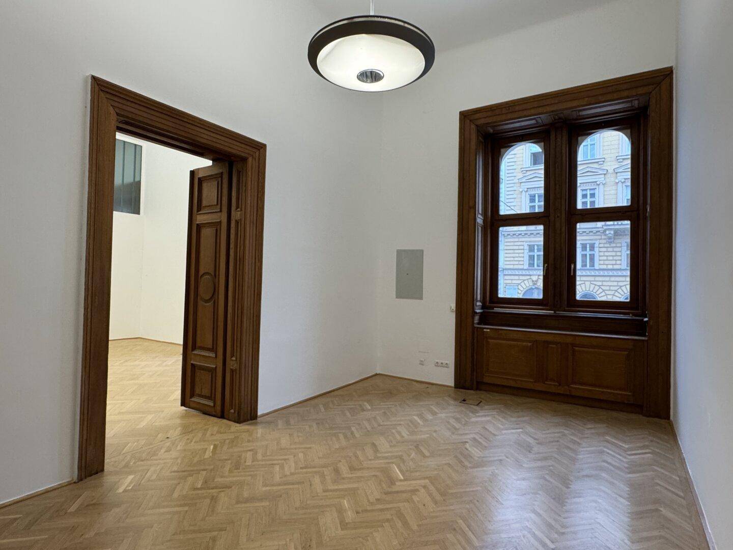 Geräumiger Raum mit Fischgrätparkett, hohen Decken und einer eleganten Holztür.