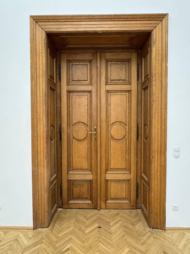 Eine imposante Doppeltür aus Holz mit aufwendigen Schnitzereien und Fischgrätparkett.